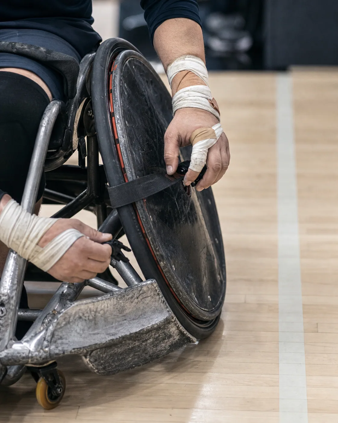 An athlete prepares a wheelchair rugby competition chair at the edge of the court.